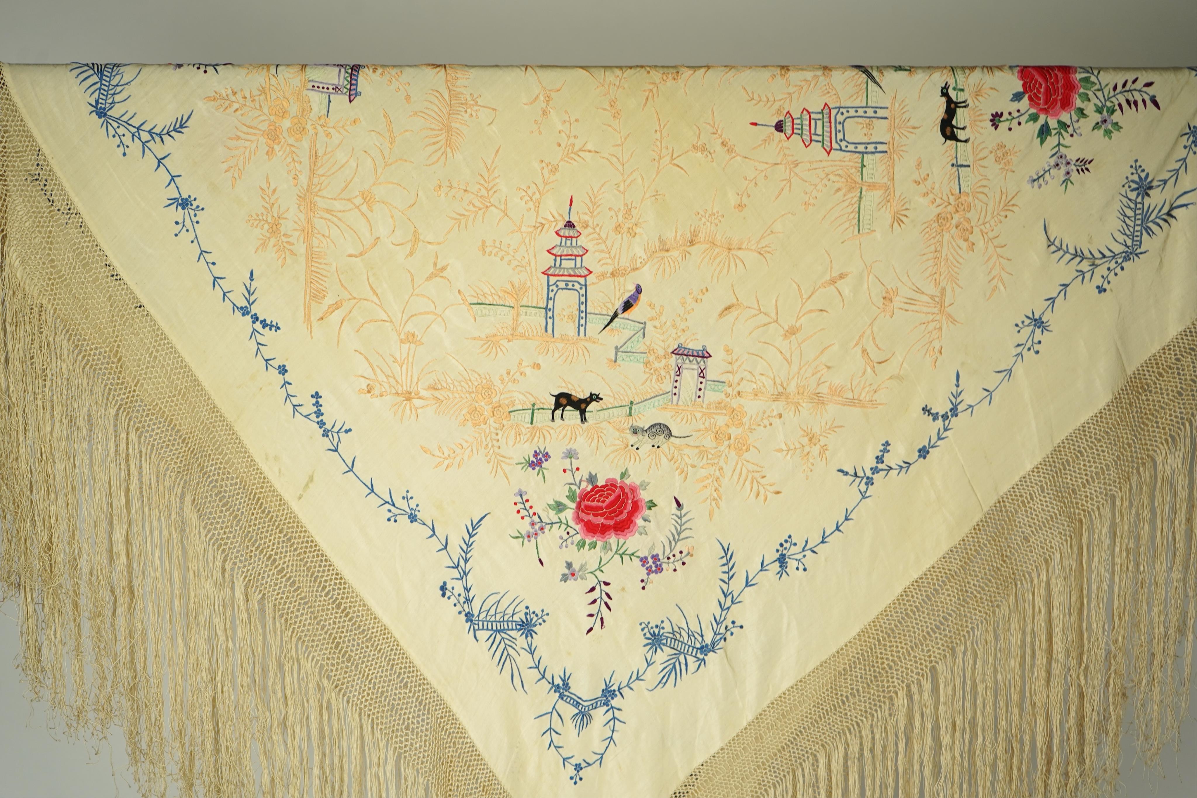 A Chinese cream silk polychrome embroidered shawl with a long fringe. Embroidered with four unusual corner cartouches of Pagoda, flowers, birds, cats and dogs. 132cm x 126cm.